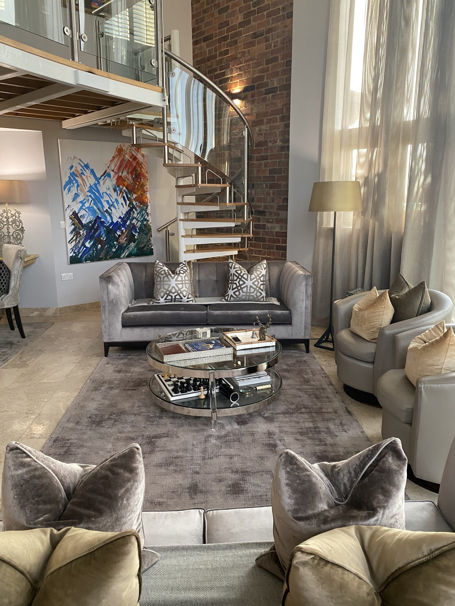 Spiral staircase rising through a double-height living room with exposed brick
